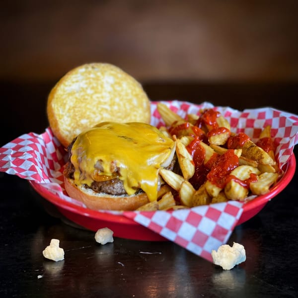 Cheeseburger with melted cheese, caramelized onions, and a side of ketchup-covered fries in a red basket.