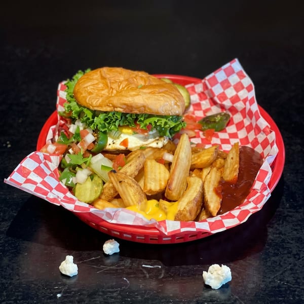 A burger with lettuce, tomato, onion, and a fried egg, served with potato wedges and sauces.